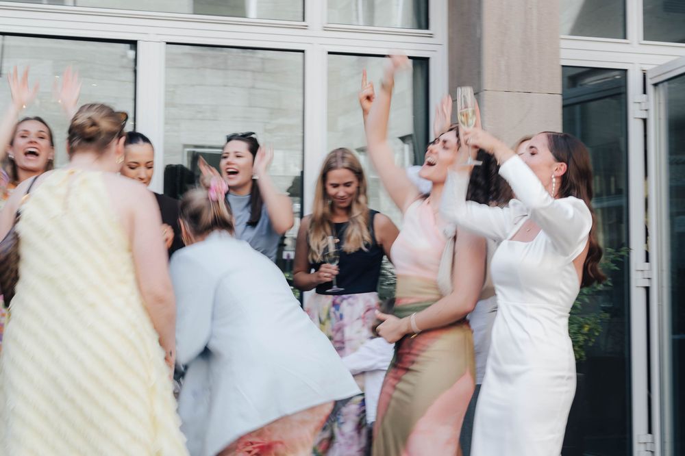 Joyful wedding guests dancing and celebrating outdoors, raising hands and laughing together at a lively reception party.