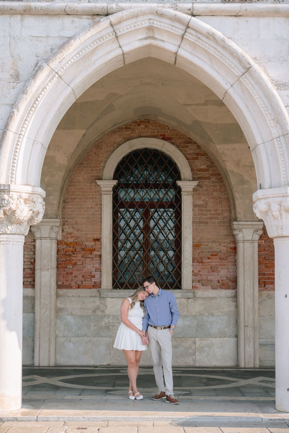 Romantic couple embracing under ornate white marble arch with brick wall and Gothic window in Venice, Italy.