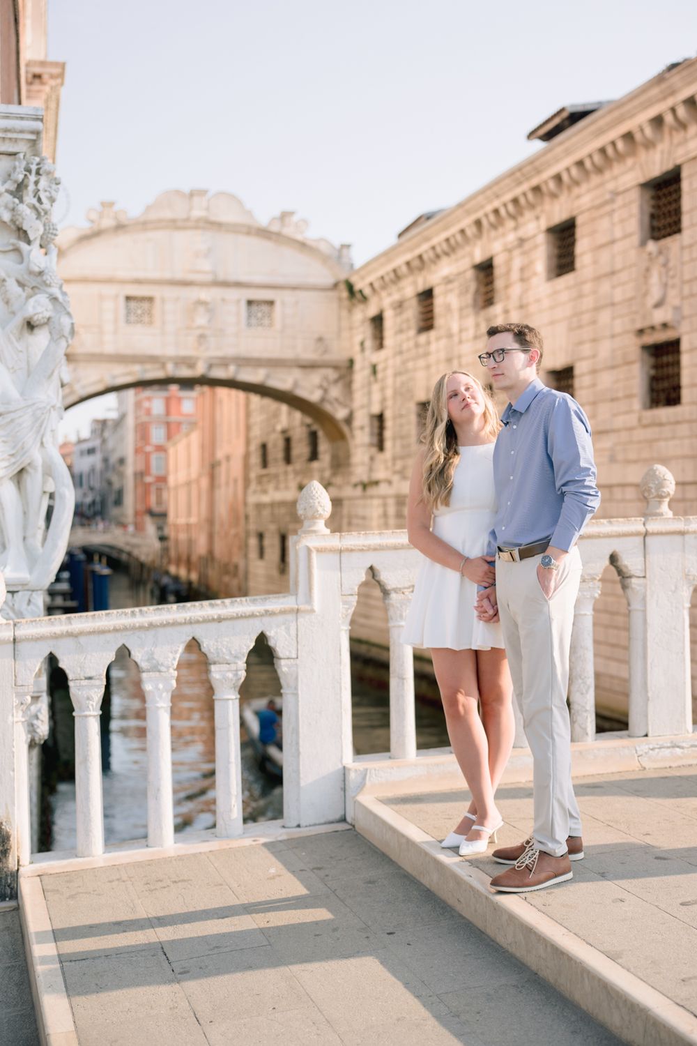 Couple posing romantically near the Bridge of Sighs in Venice, Italy, on a sunny day.