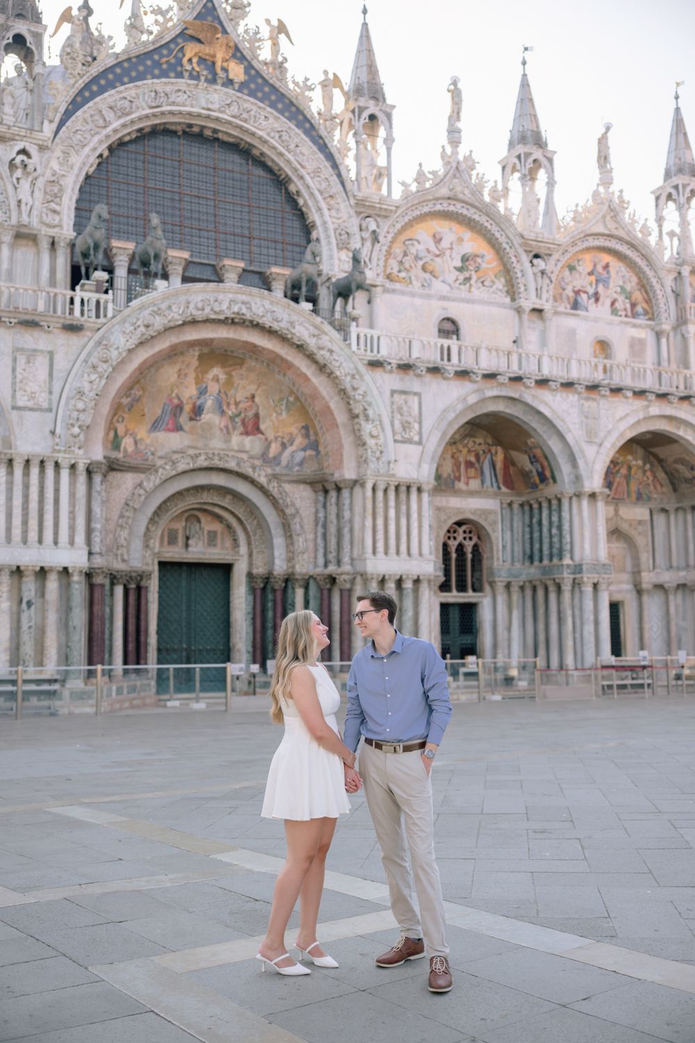 Couple holding hands before the ornate facade of St. Mark's Basilica in Venice.