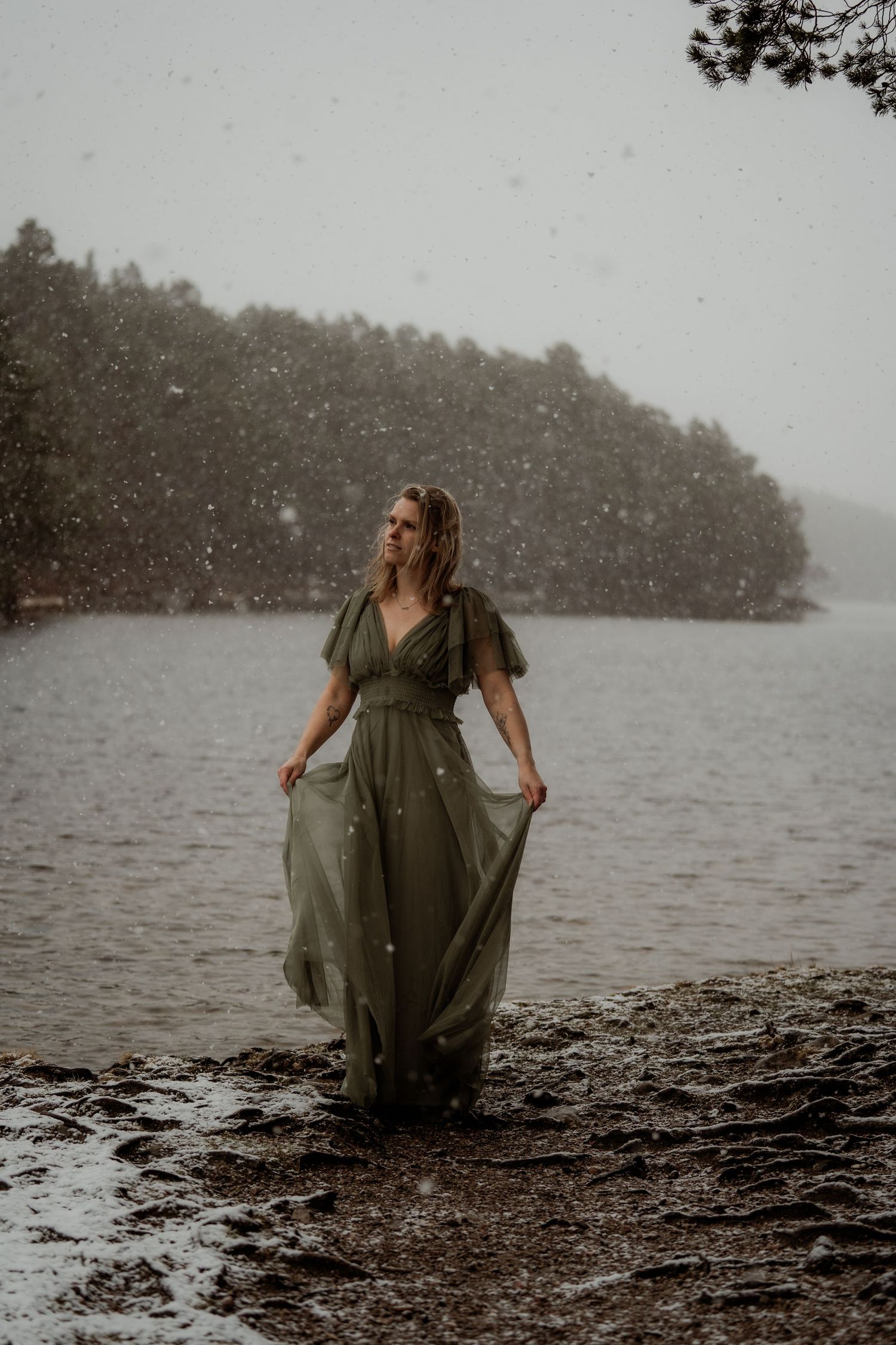 Woman in flowing green dress twirls before a misty mountain in a dramatic Scottish Highland landscape.