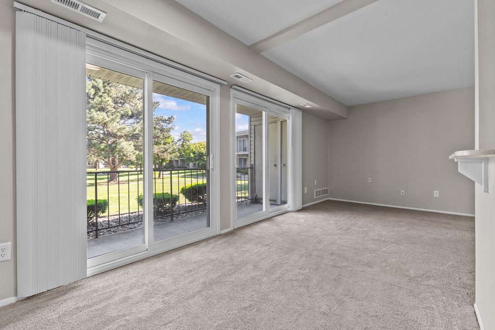Bright living room with vaulted ceiling, plush carpet, and sliding glass doors opening to a balcony with outdoor seating.