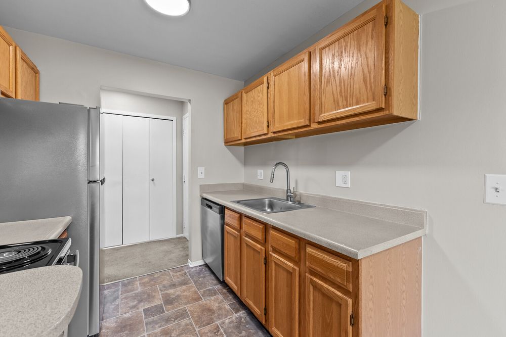 Modern kitchen with oak cabinets, stainless steel sink, tile flooring, and adjacent closet with white door.