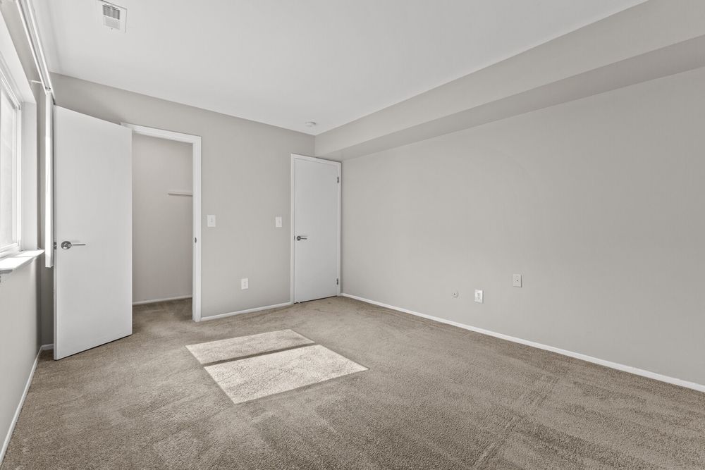 Empty bedroom featuring gray carpet, neutral walls, two doors leading to closets, and soft natural light.