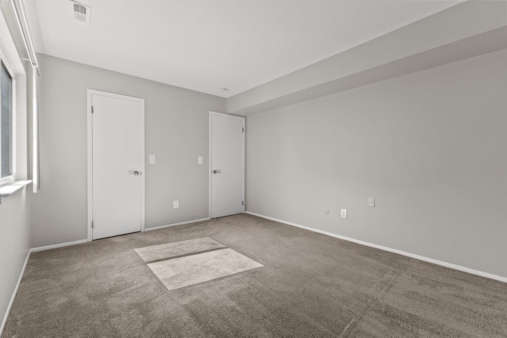 Empty bedroom with gray carpet, two white doors, and neutral gray walls in a modern apartment.
