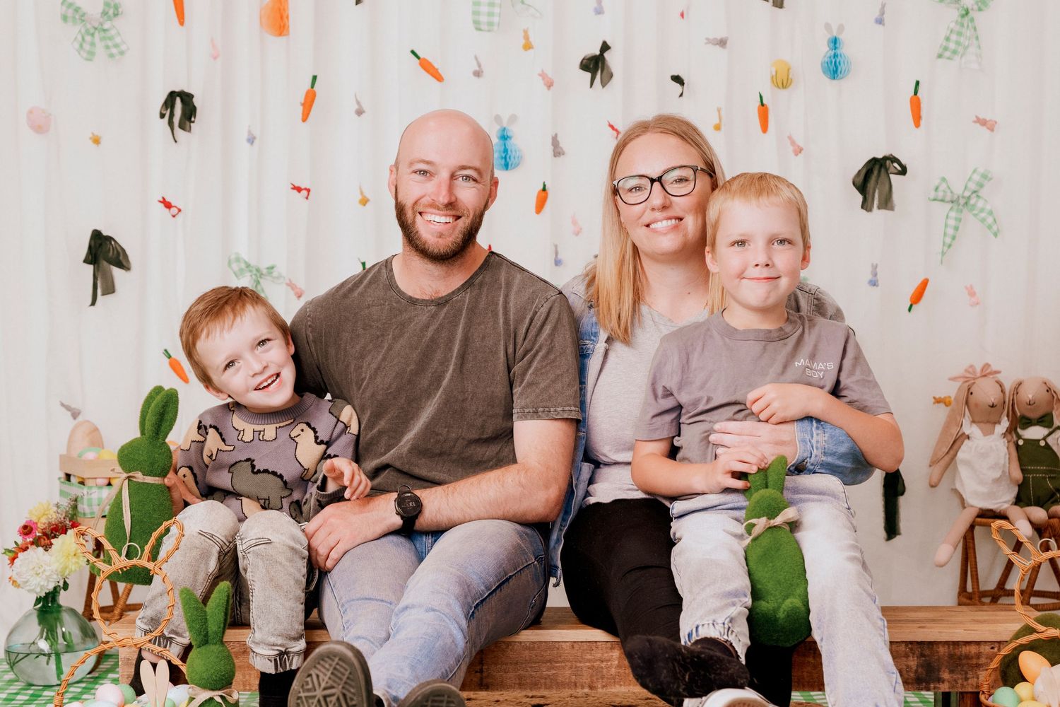 Happy family of four posing for Easter mini session with festive bunny decorations and spring backdrop.