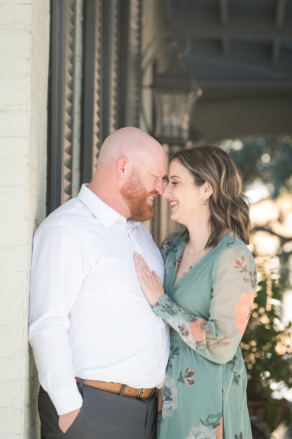 A smiling couple in romantic embrace, woman in floral green dress with hand on mans white shirt outdoors.