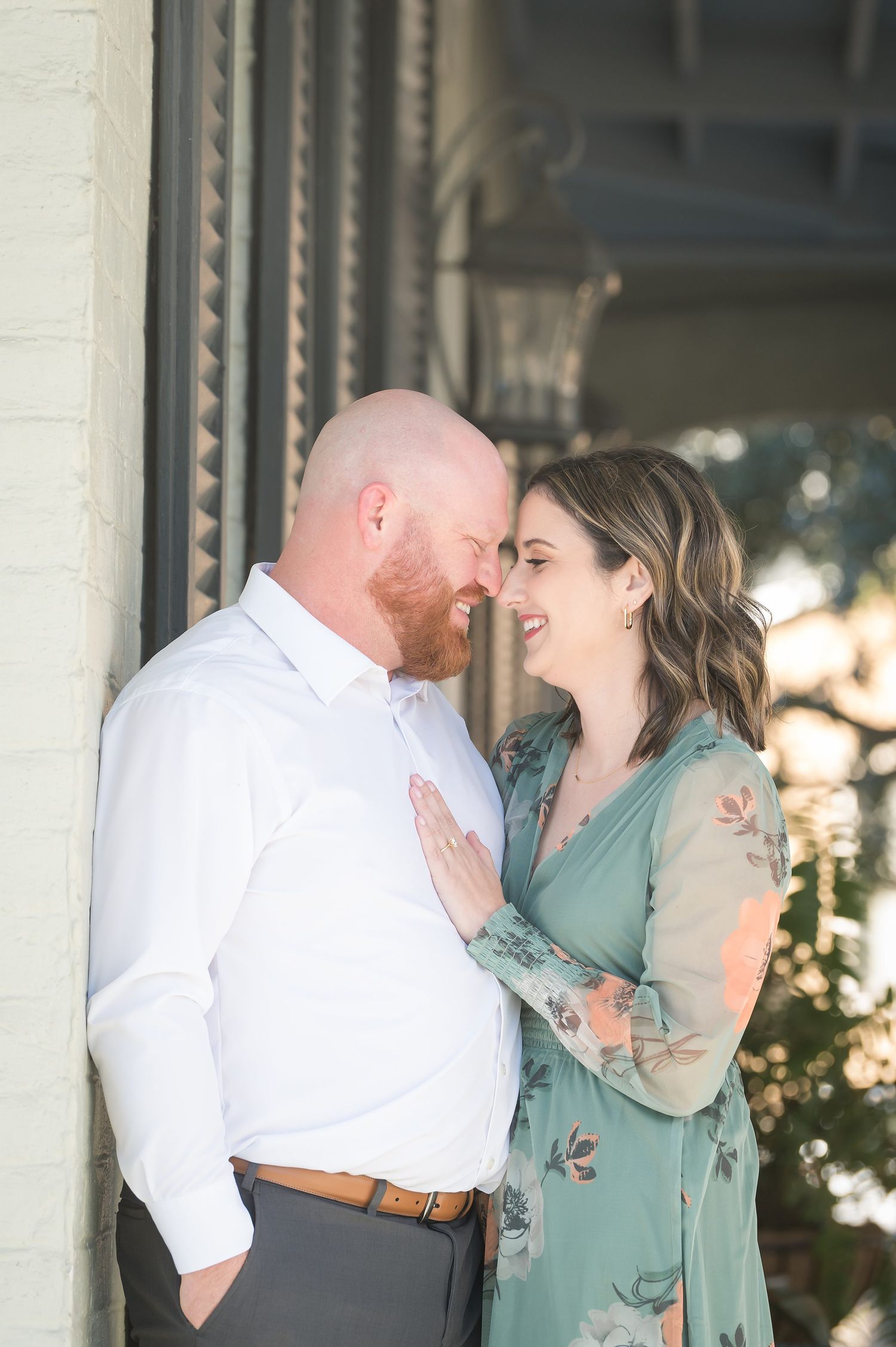 A smiling couple in romantic embrace, woman in floral green dress with hand on mans white shirt outdoors.