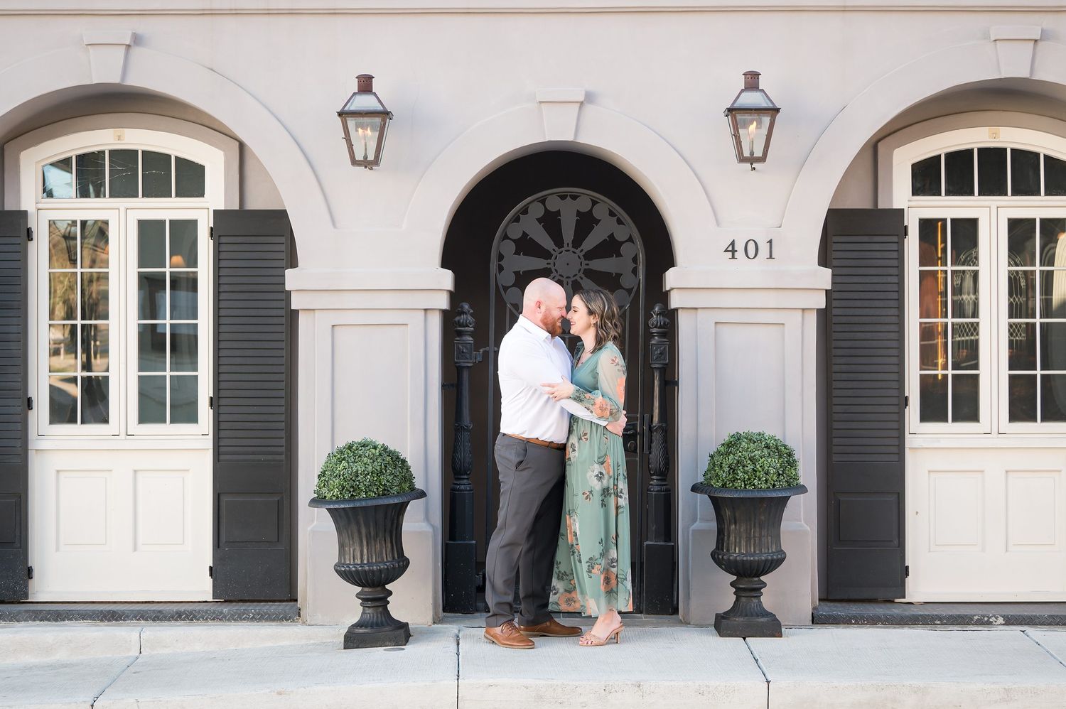 Couple sharing a romantic kiss in front of elegant building entrance numbered 401 with black doors and lanterns.