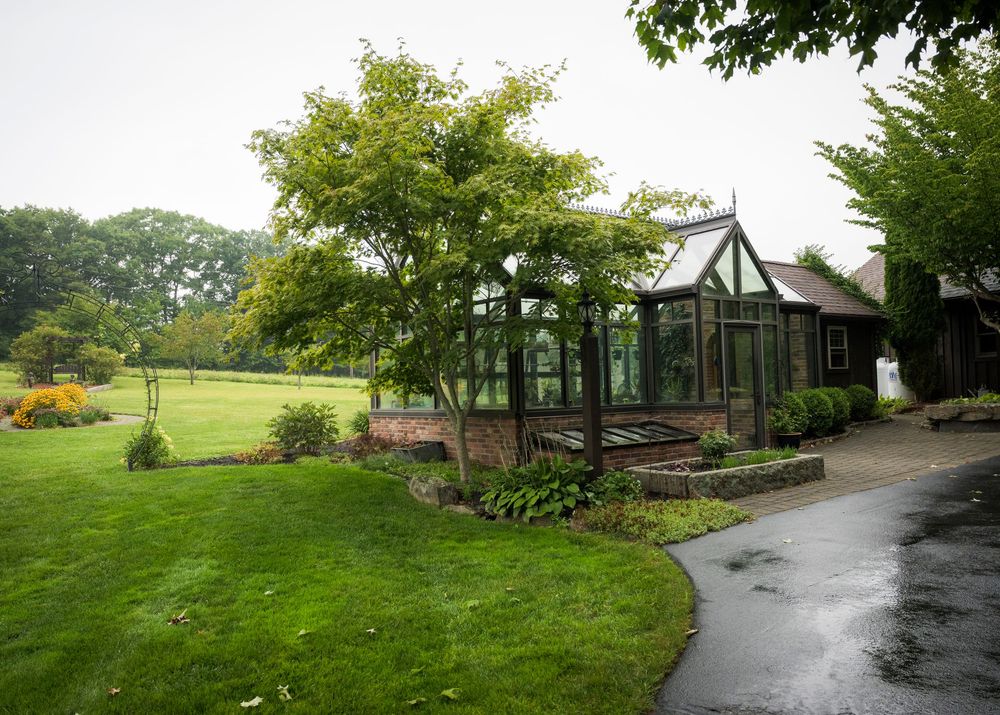 Lush green garden with a glass greenhouse, curved pathway, and manicured lawn on a cloudy day.