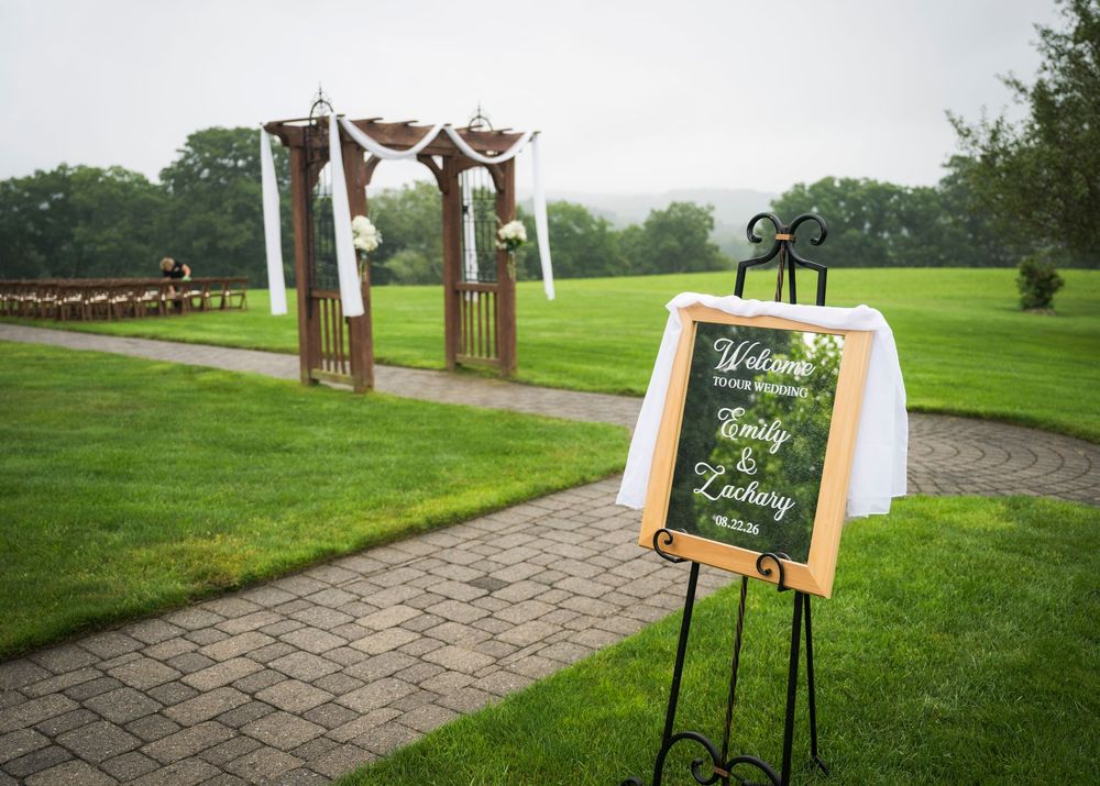 Outdoor wedding ceremony setup with chalkboard welcome sign for Emily and Zachary on a lush green lawn.