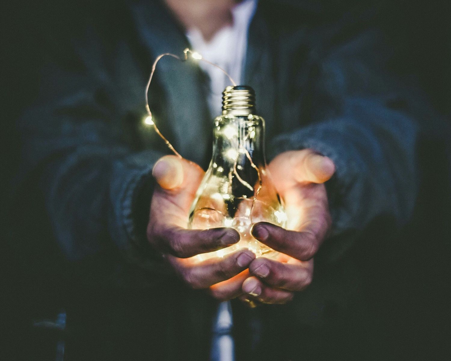 Hands cupping a glowing light bulb with fairy lights, symbolizing creativity and innovation.