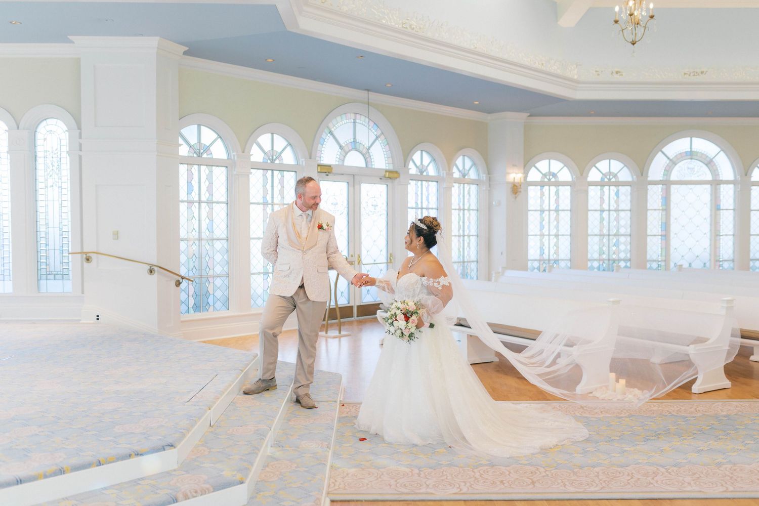 Bride and groom share a tender first look moment in an elegant white wedding chapel with arched windows.