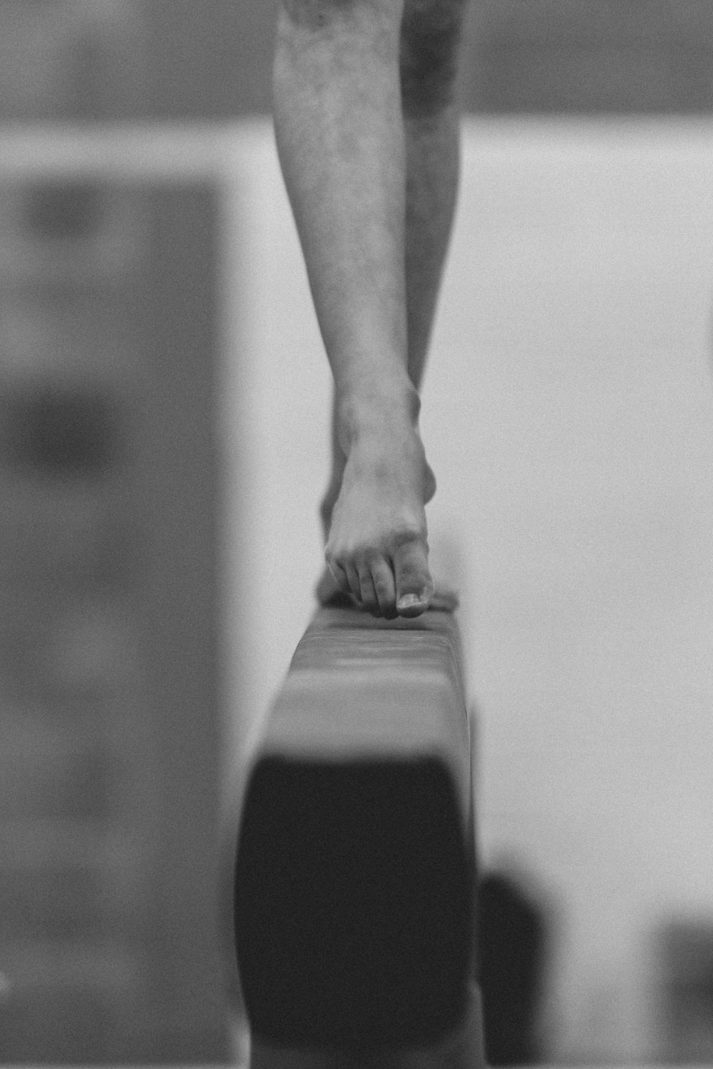 Closeup black and white photograph showing a gymnast's foot balancing on a beam during practice or competition.