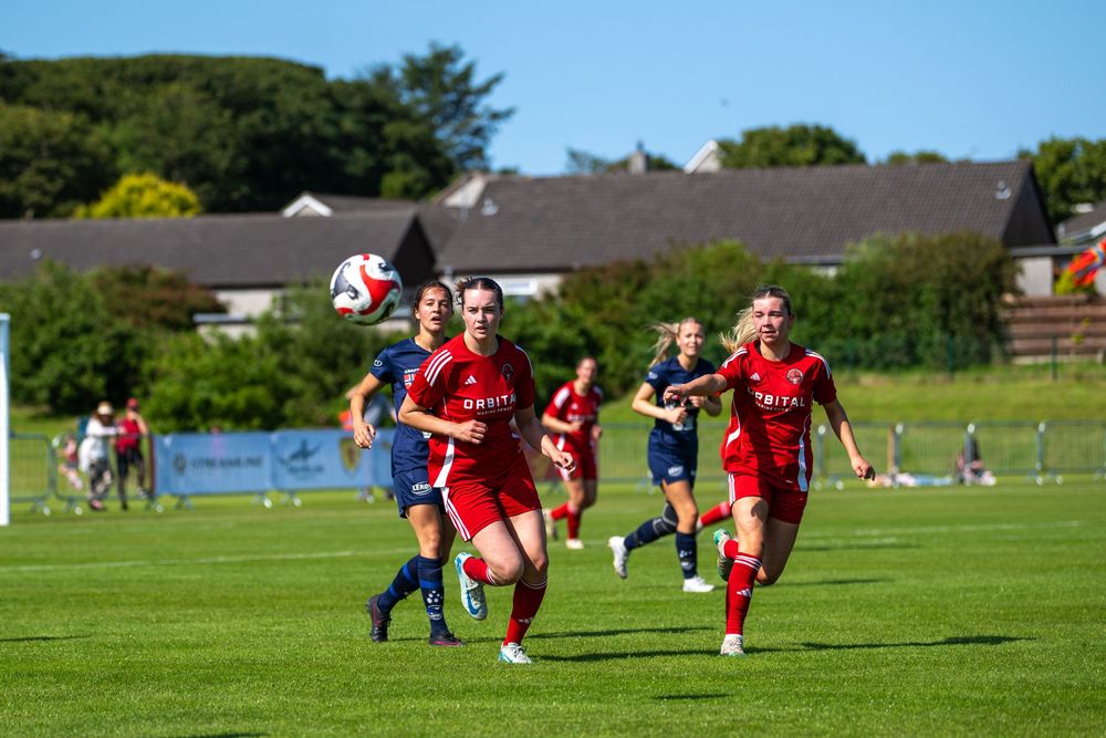 Youth soccer players in red uniforms compete on a sunny grass field during a match.