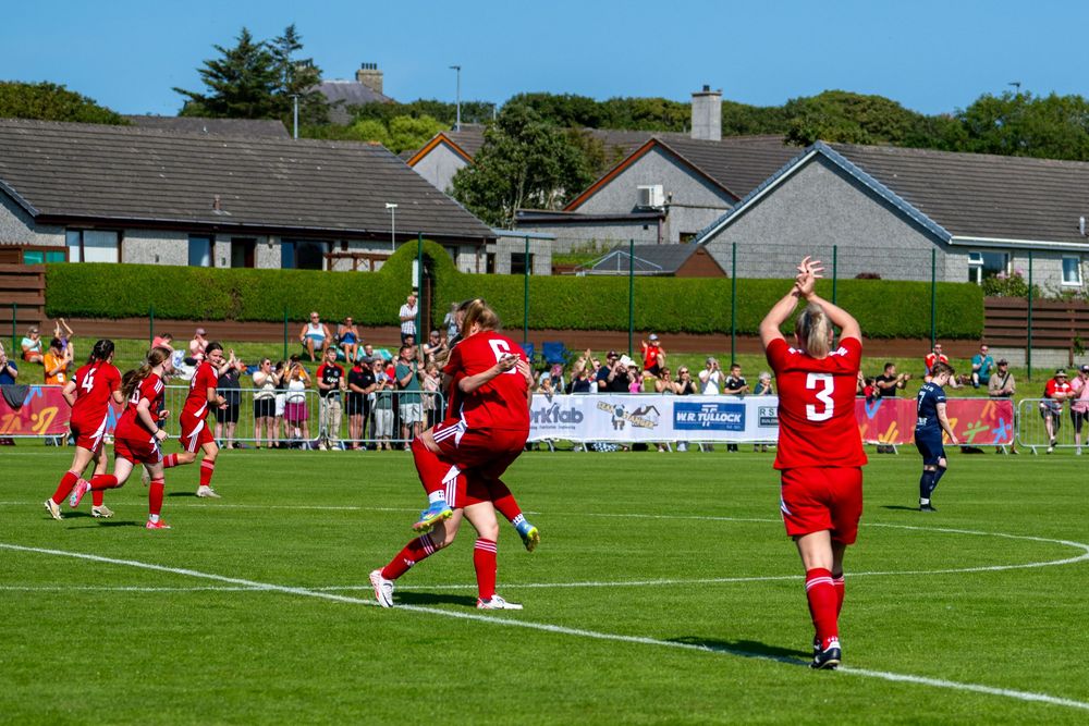 Rugby players in red uniforms compete against opponents during a match on a green grass field.