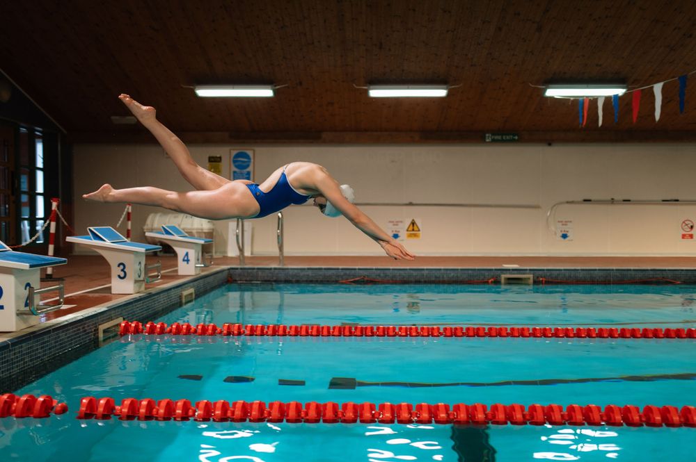 A swimmer in a blue swimsuit dives gracefully into a competition pool with red lane dividers.