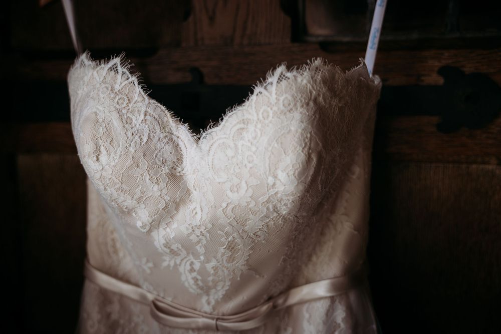 Close-up of an ivory lace sweetheart wedding dress with satin ribbon belt hanging in soft light.