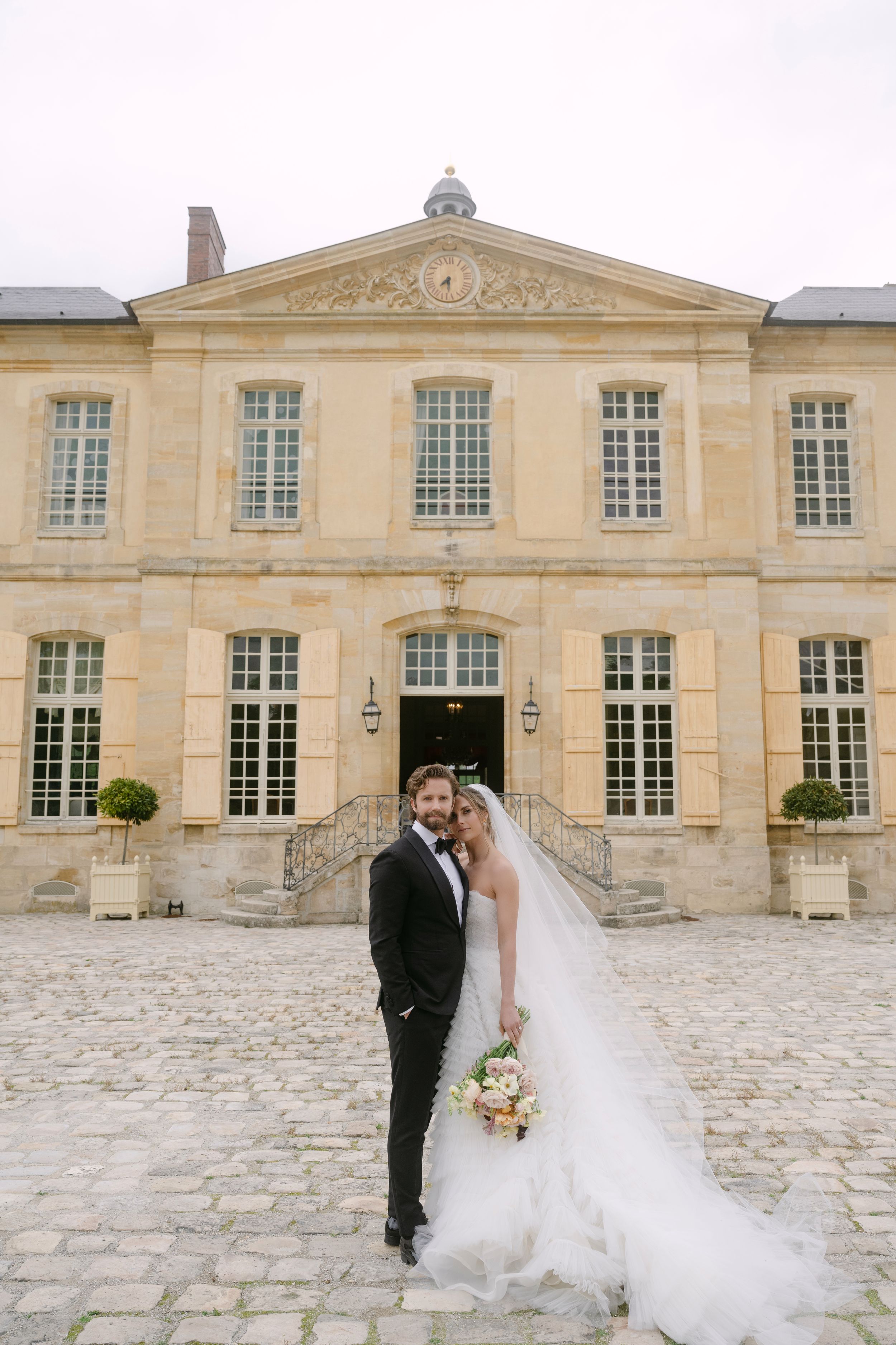Bride and groom pose in front of a grand French chateau on their wedding day.