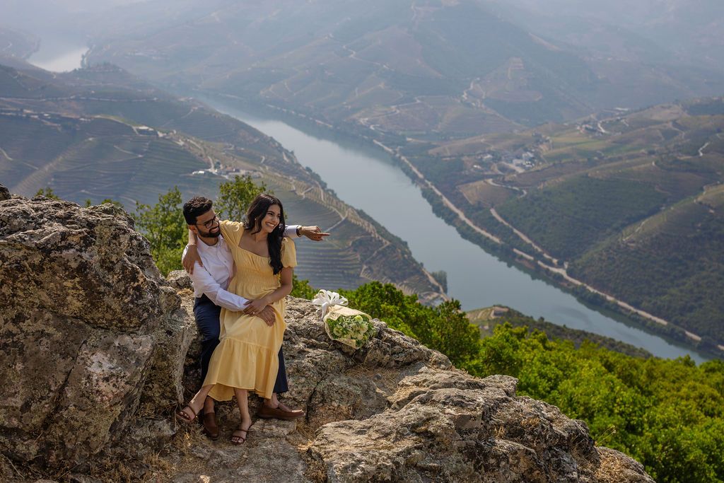 Couple embracing on rocky hilltop overlooking scenic Douro River valley with terraced vineyards in Portugal.