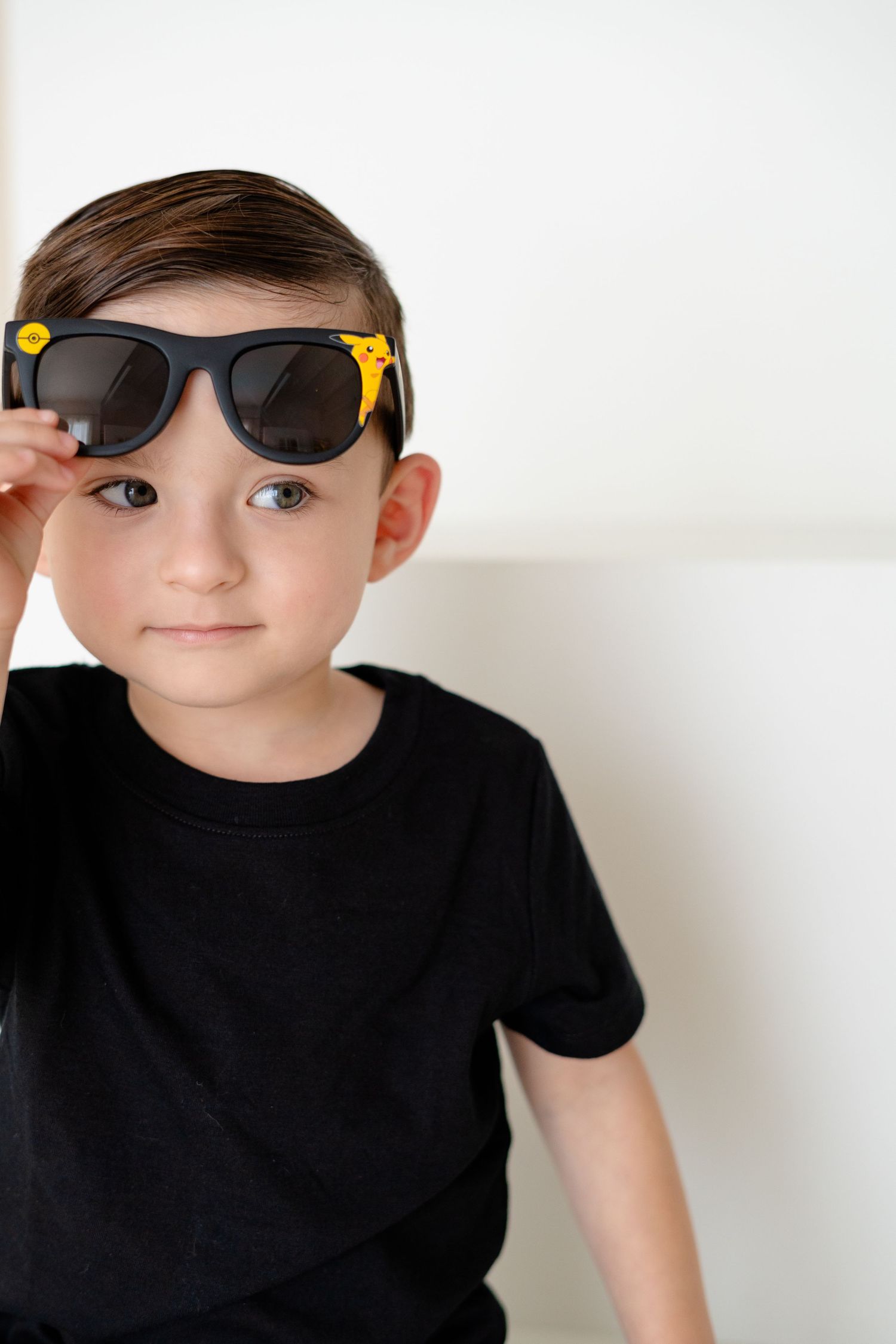 Young boy in black t-shirt wearing oversized black and yellow sunglasses, posing confidently against a white background.