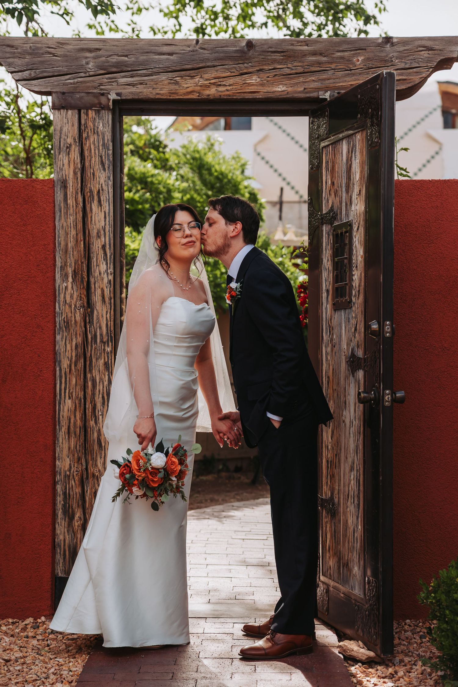 Bride and groom sharing a romantic kiss surrounded by lush tropical gardens with blue flowers.