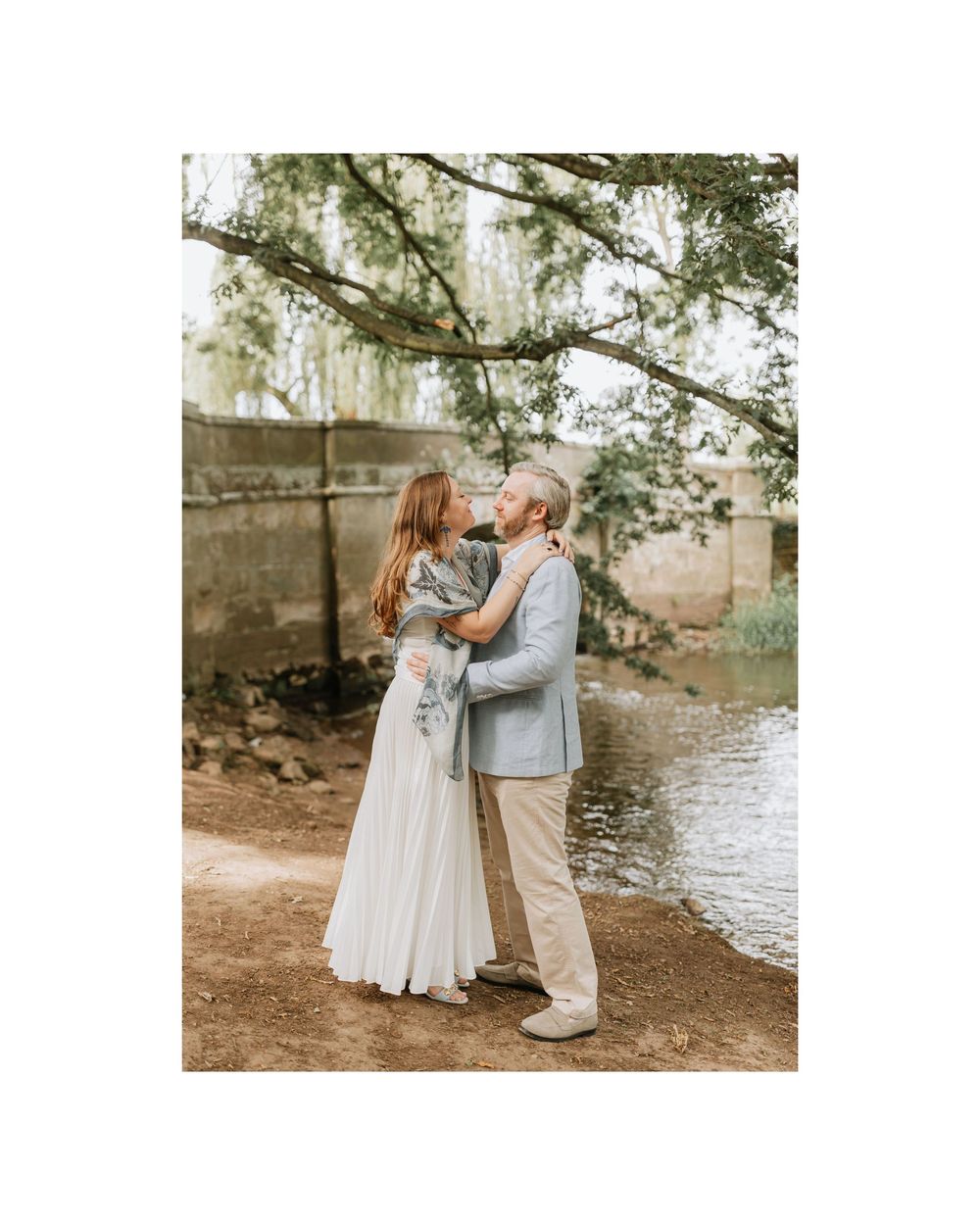 Couple sharing a tender kiss near a serene river under a canopy of trees during their wedding.