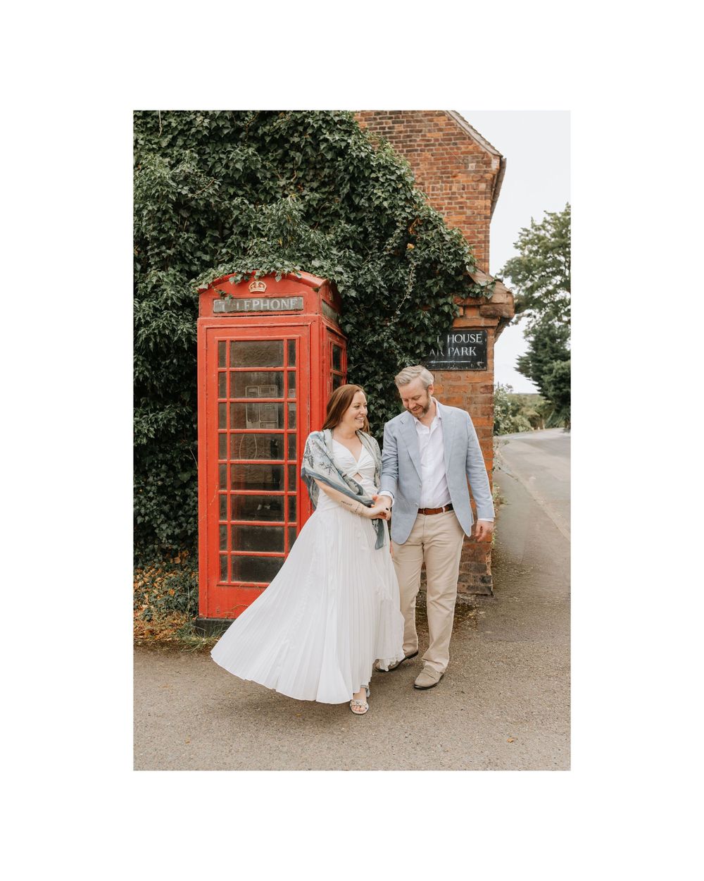 Happy couple walking and laughing together beside iconic red British telephone box on country road.