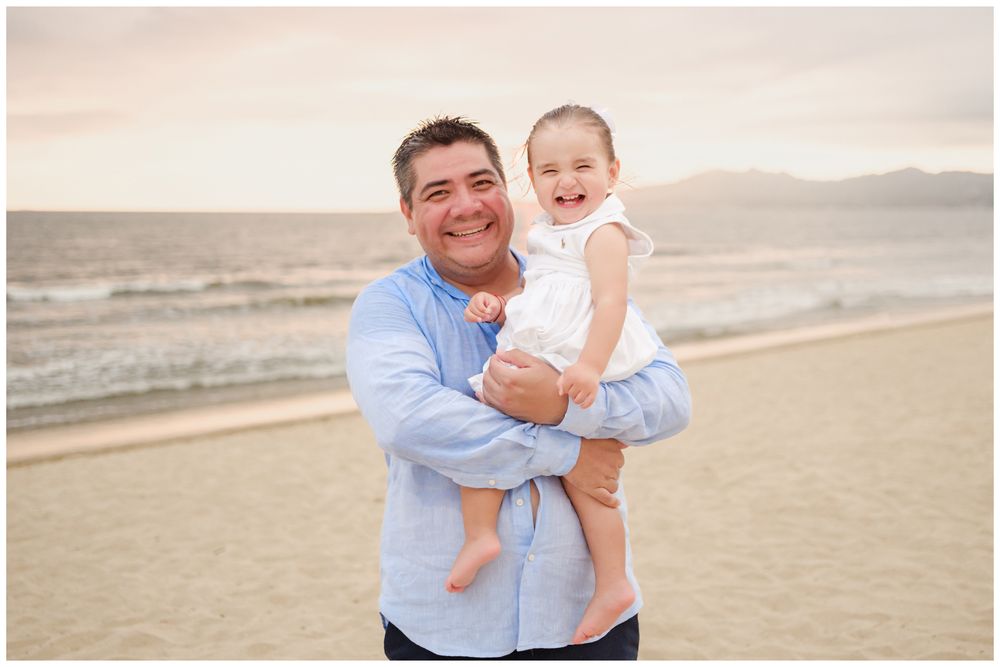 Father holding his smiling daughter on a Punta Mita beach at sunset, candid family photography with ocean views in Mexico.