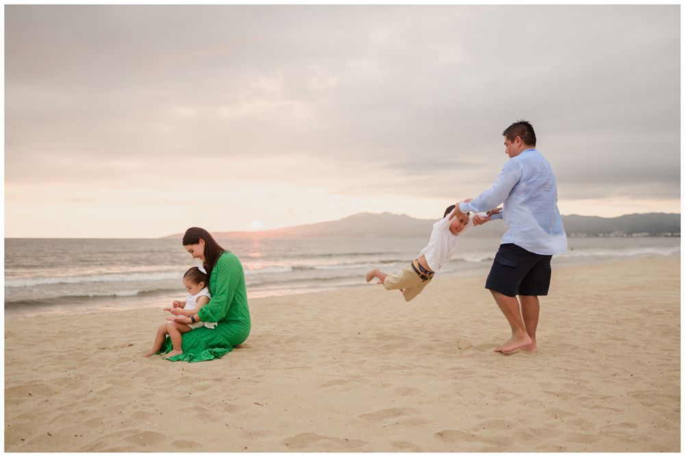 Family of four at sunset on a Punta Mita beach, father swinging child during a candid family photography session in Mexico.