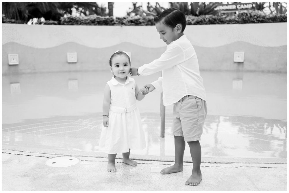 Black and white portrait of siblings holding hands by a Punta Mita resort pool, candid family photography Riviera Nayarit.