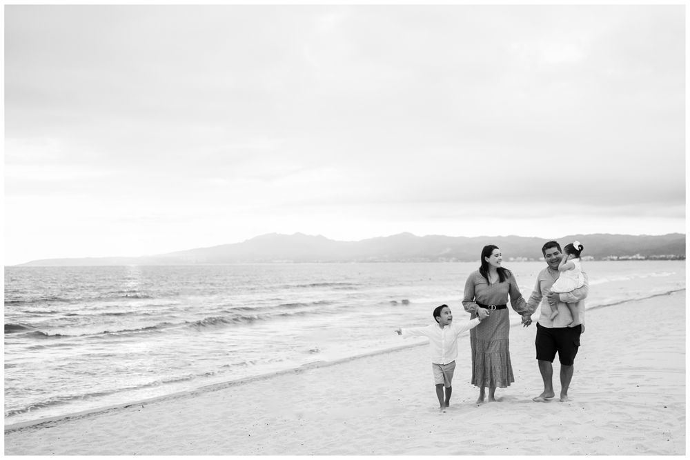 Black and white family walking hand in hand on a Punta Mita beach, candid family photography Riviera Nayarit.