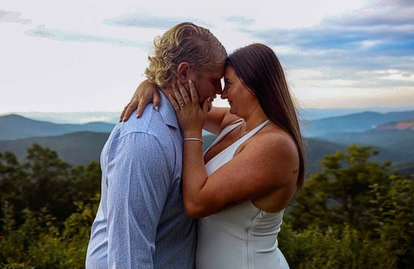 Couple sharing a romantic moment at sunset with dramatic clouds and mountain views in the background.
