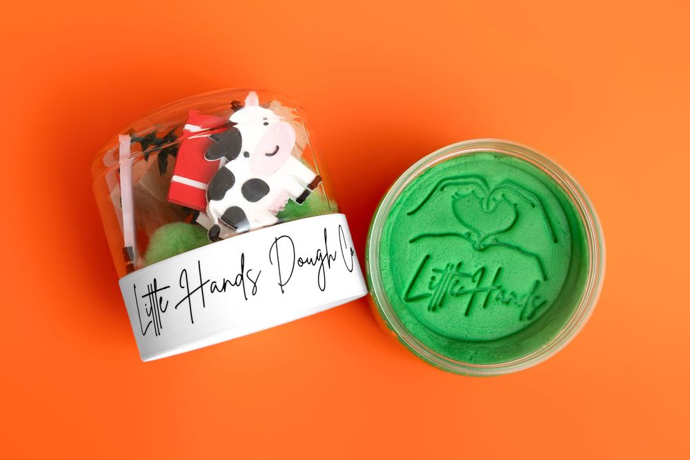 Little Hands Dough kit with cow figurine and green play dough in clear container on orange background.