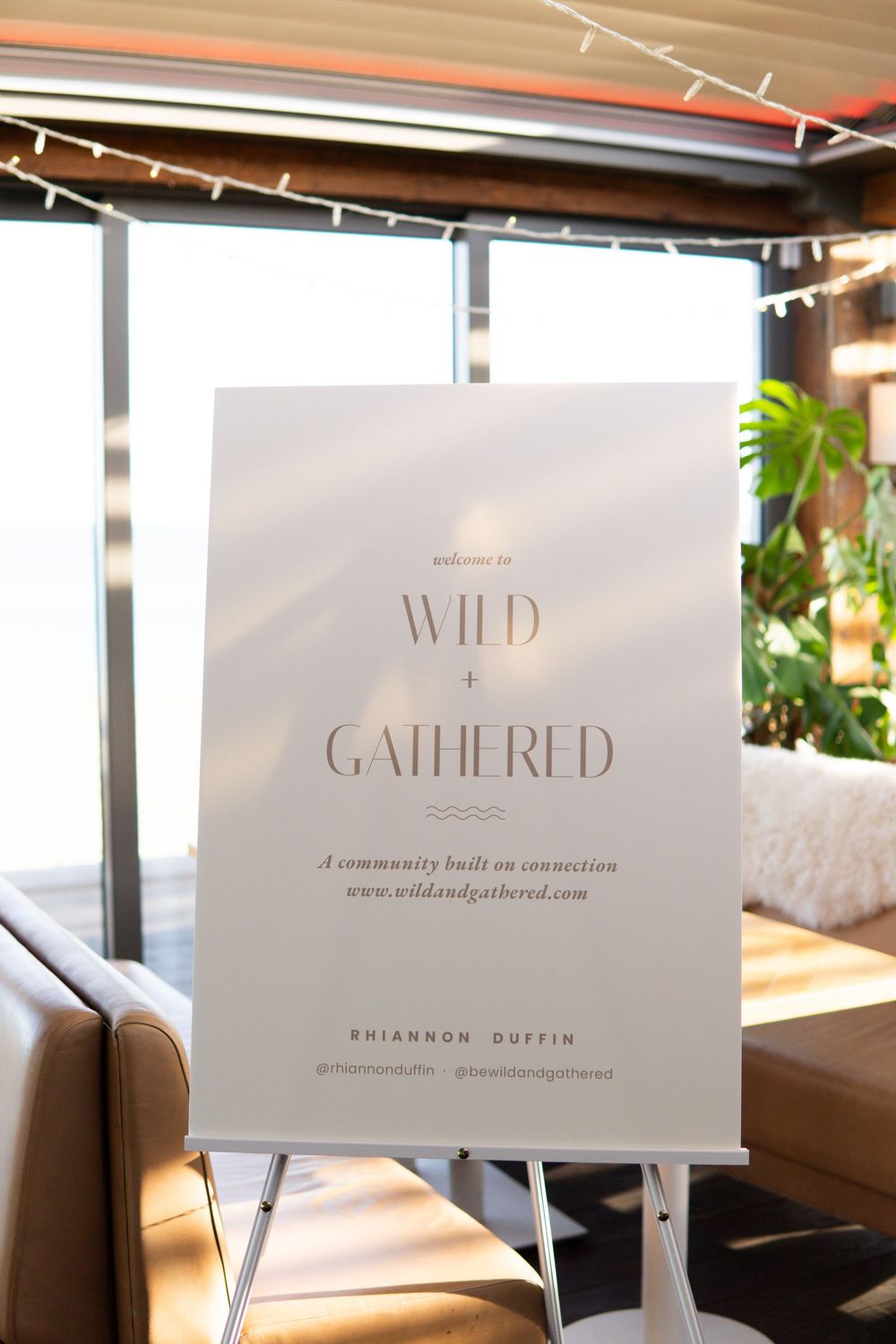 White welcome sign for Wild + Gathered community event on easel in bright modern venue.