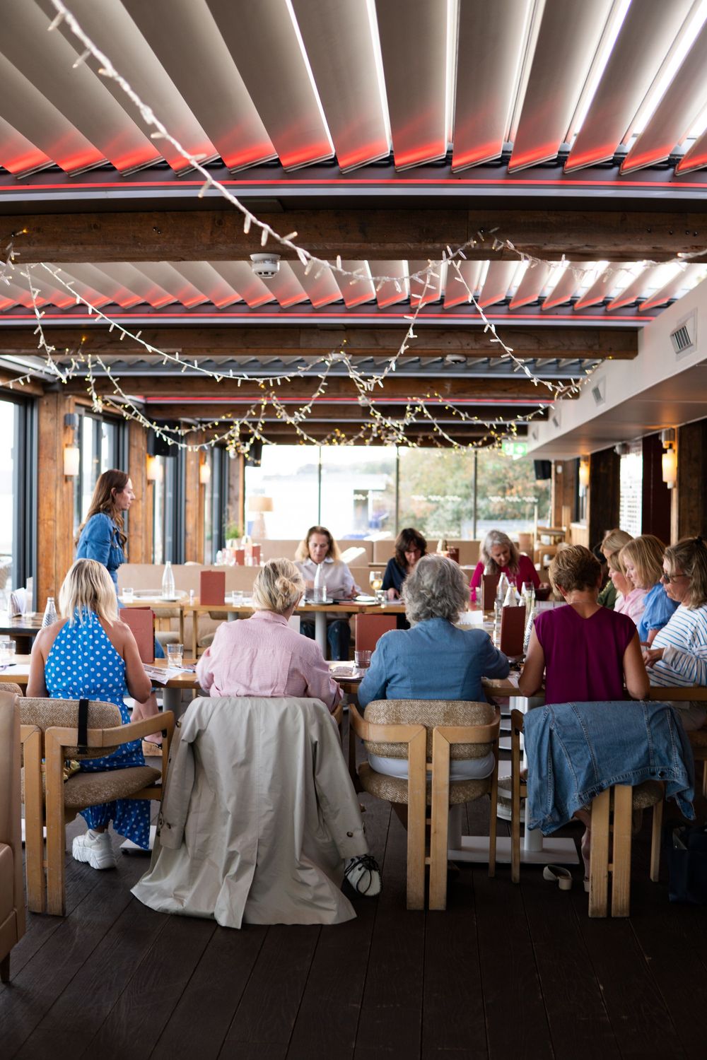 Groups of people dining together in a warmly lit restaurant decorated with string lights and wooden furniture.