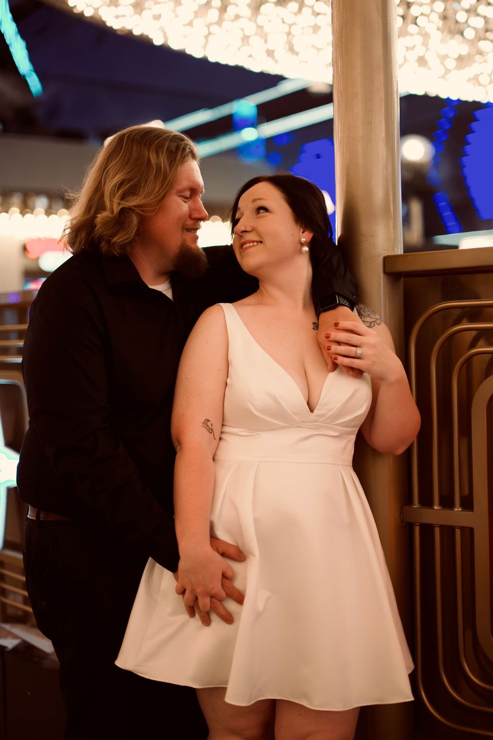 Newlyweds posing together near a gold pillar with bokeh lights in a festive venue.