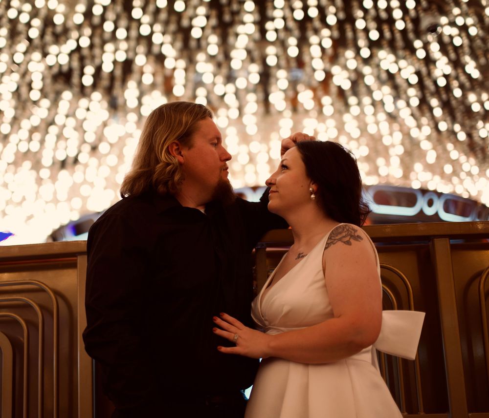 Newlywed couple gazing lovingly at each other under sparkling chandelier lights.