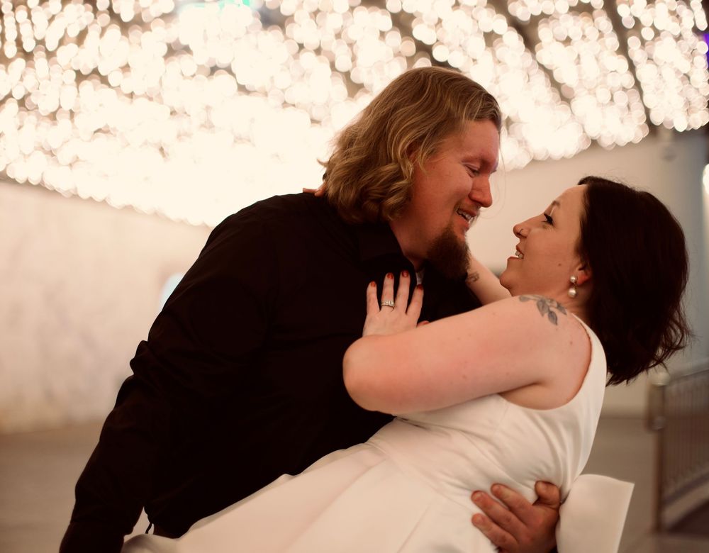 Two brides share a romantic dip dance embrace under sparkling chandelier lights at their wedding reception.