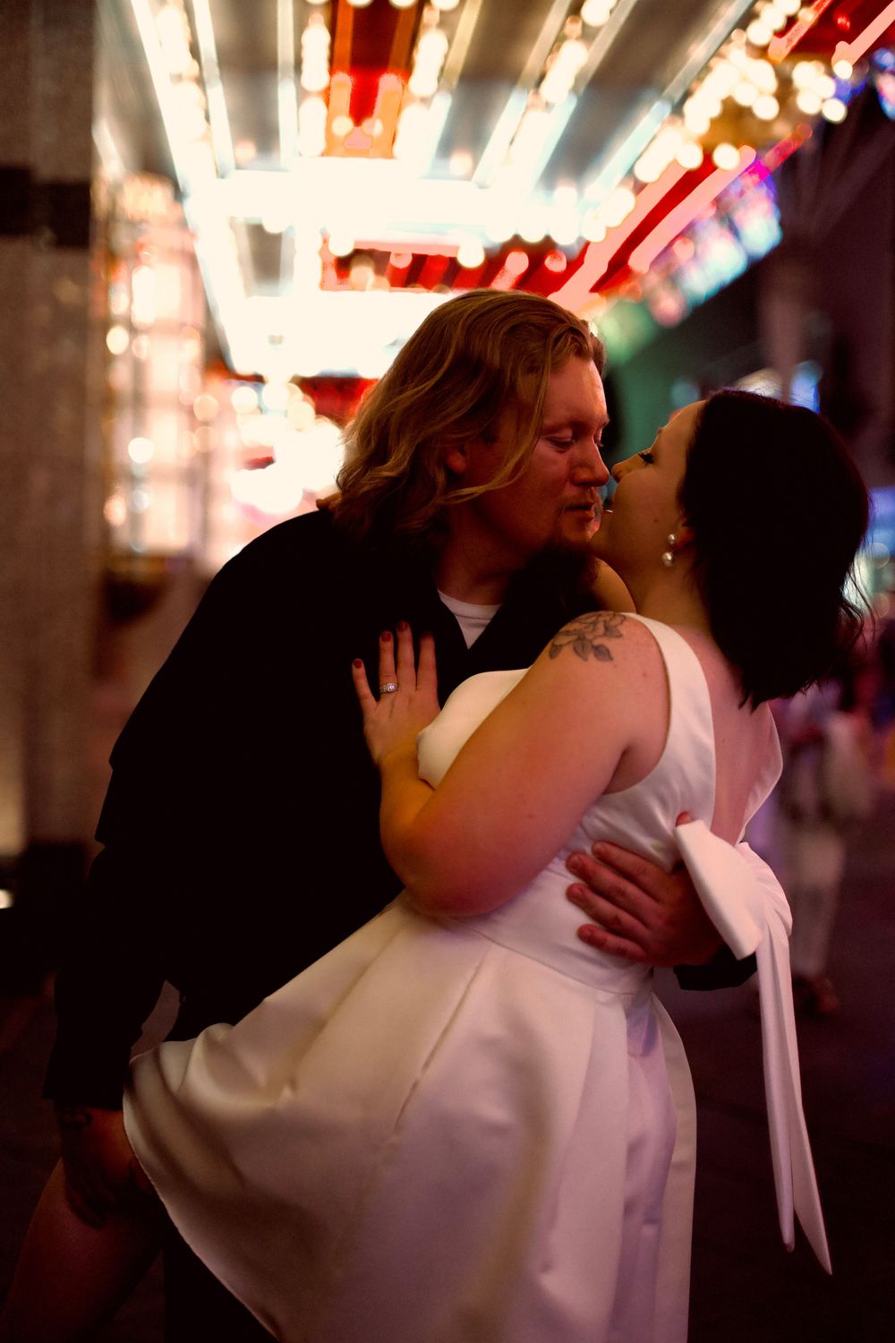 Couple sharing a romantic kiss under vibrant neon lights on the Fremont Street Experience in Las Vegas.