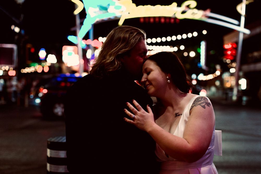 Couple sharing romantic moment on Las Vegas Strip at night, surrounded by glowing neon signs.