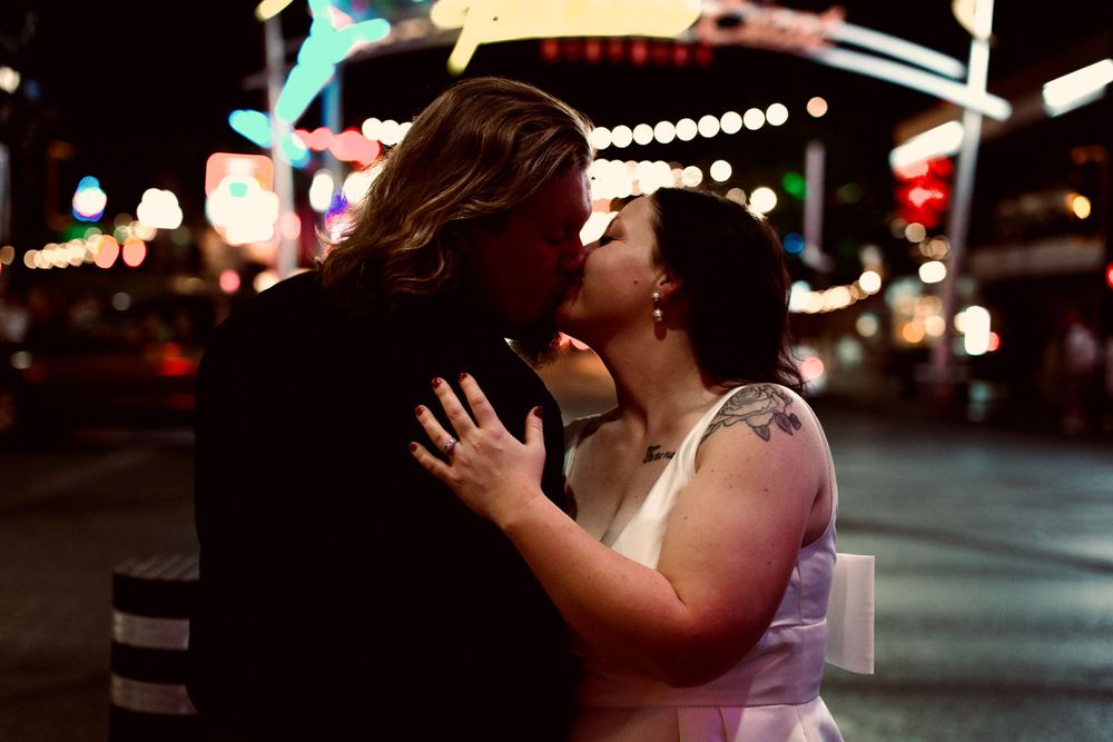 Couple sharing a romantic kiss on the Las Vegas Strip at night with colorful neon lights glowing in the background.