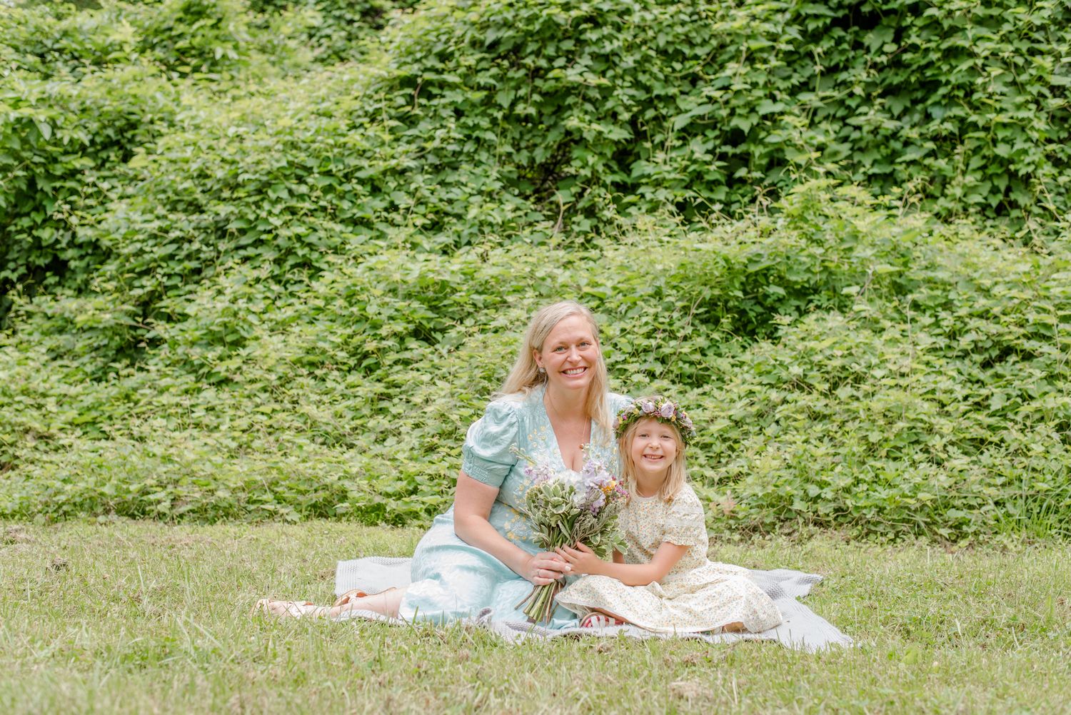 Full family photography session in Northern Virginia, mother and daughter hold bouquet together, sitting on a blanket in the grass