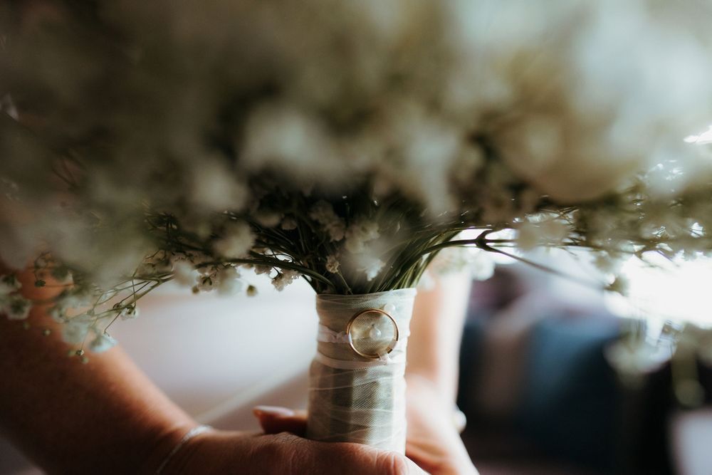 Close-up of a wedding bouquet with white baby's breath flowers, wrapped in ribbon, with a ring resting on the stems.