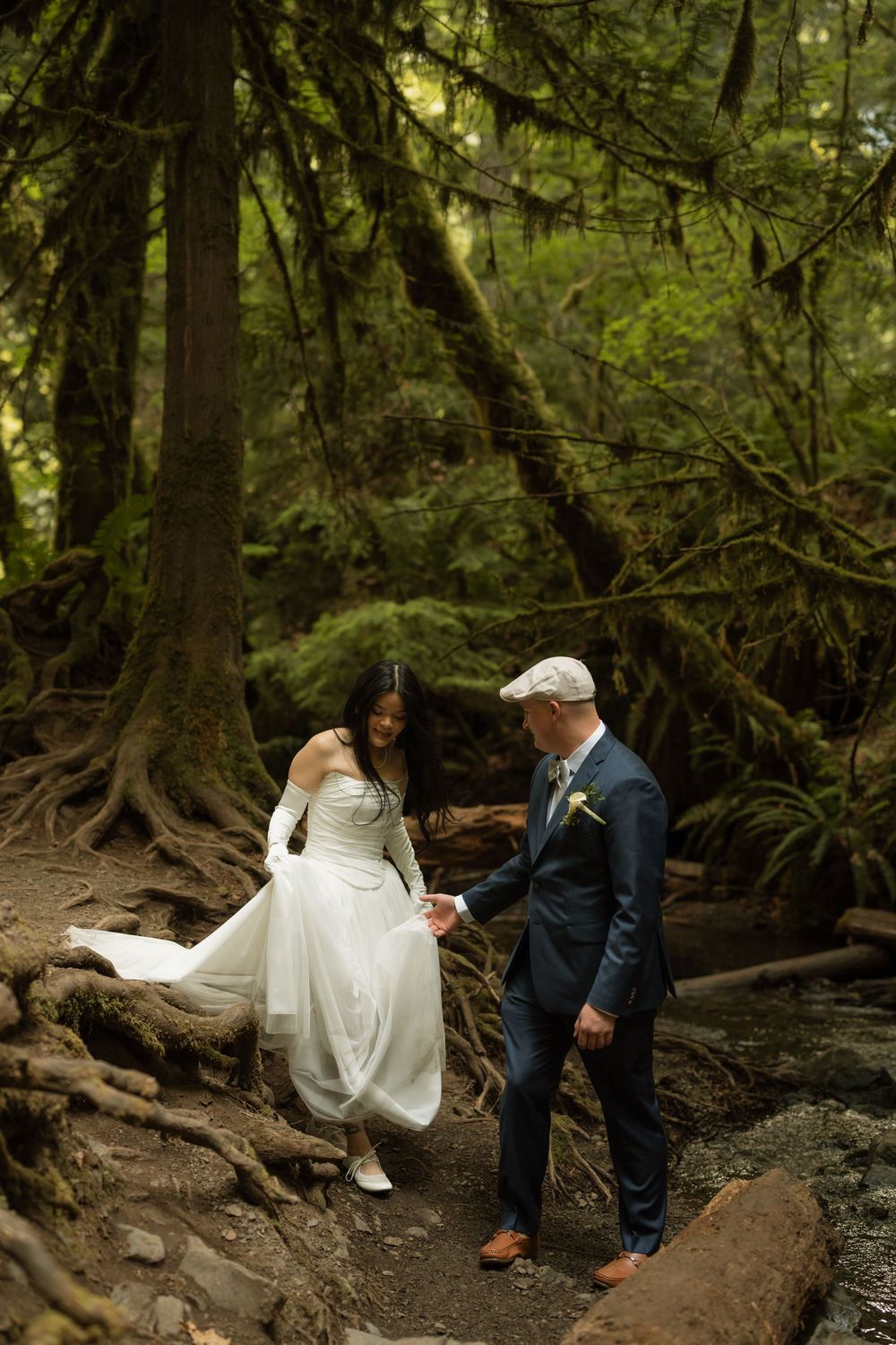 Bride and groom hold hands walking through a lush forest on their wedding day.