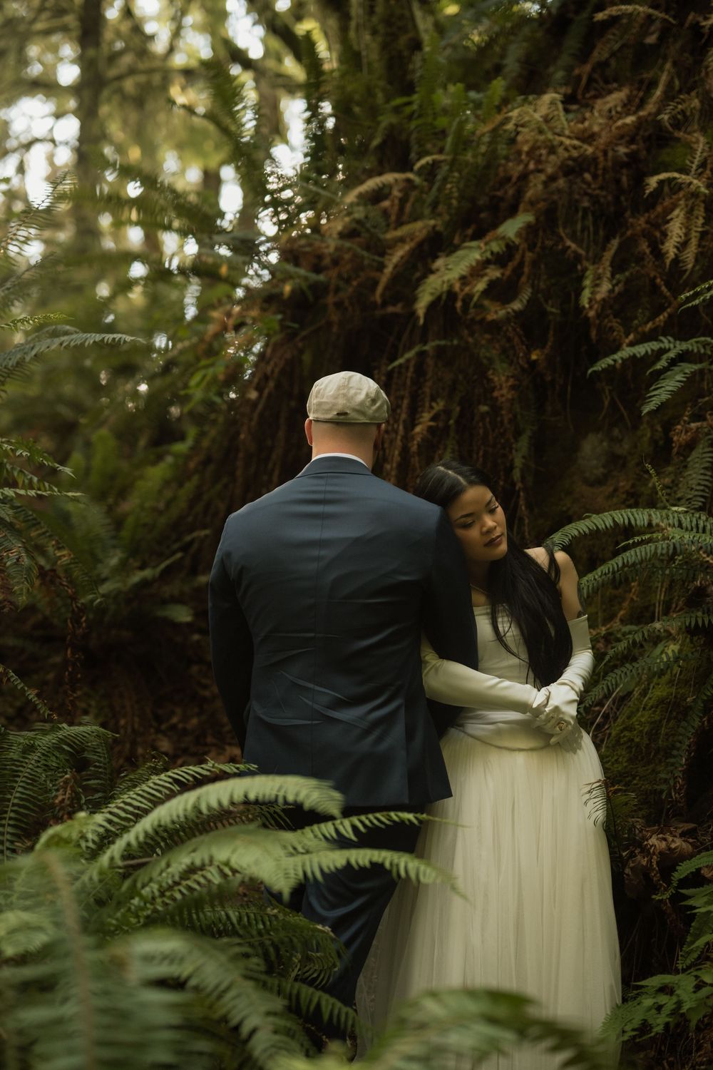 Bride and groom embrace among lush ferns in a forest wedding photo.