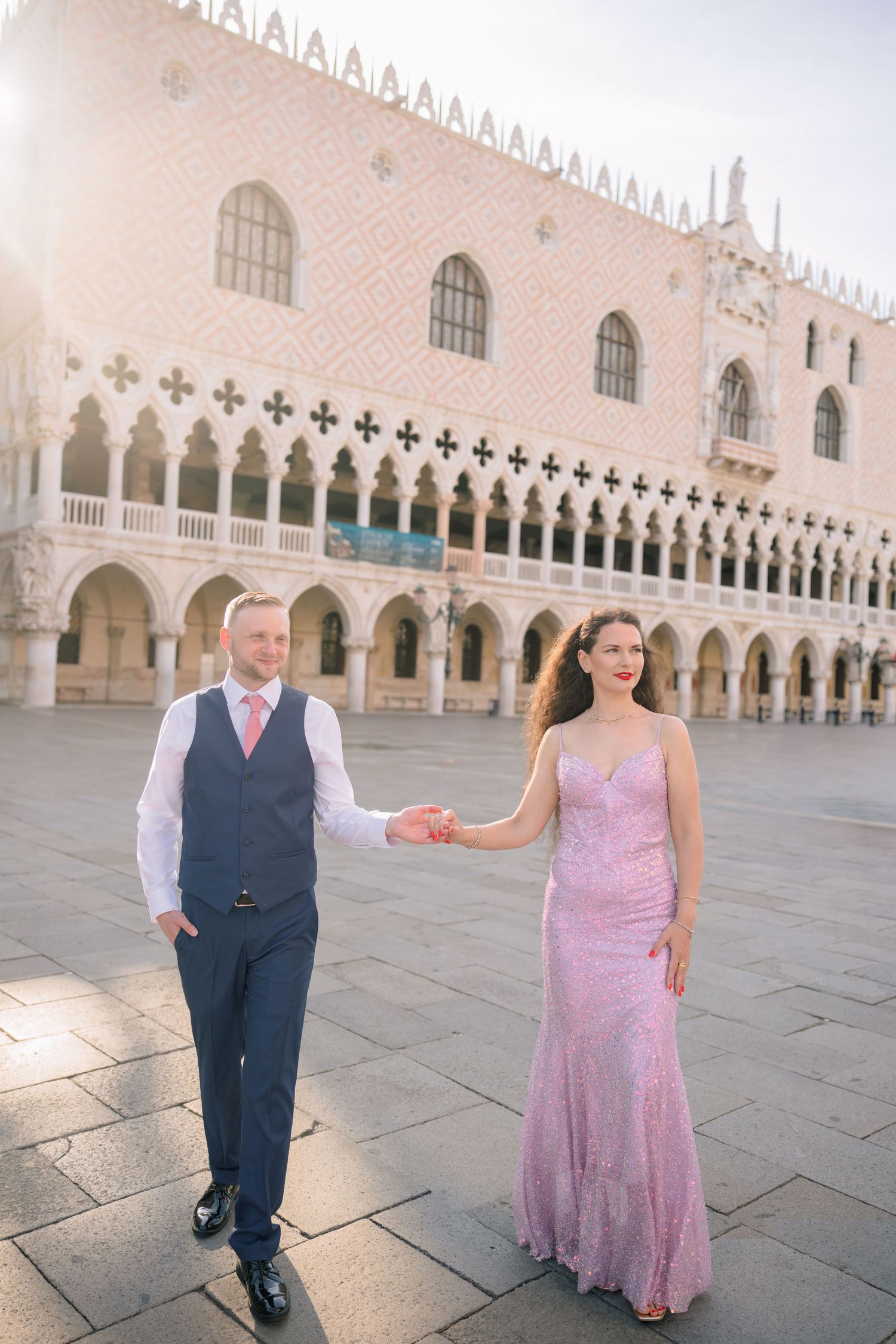 Couple in formal attire holding hands in St. Mark's Square, Venice, with the Doge's Palace in the background.
