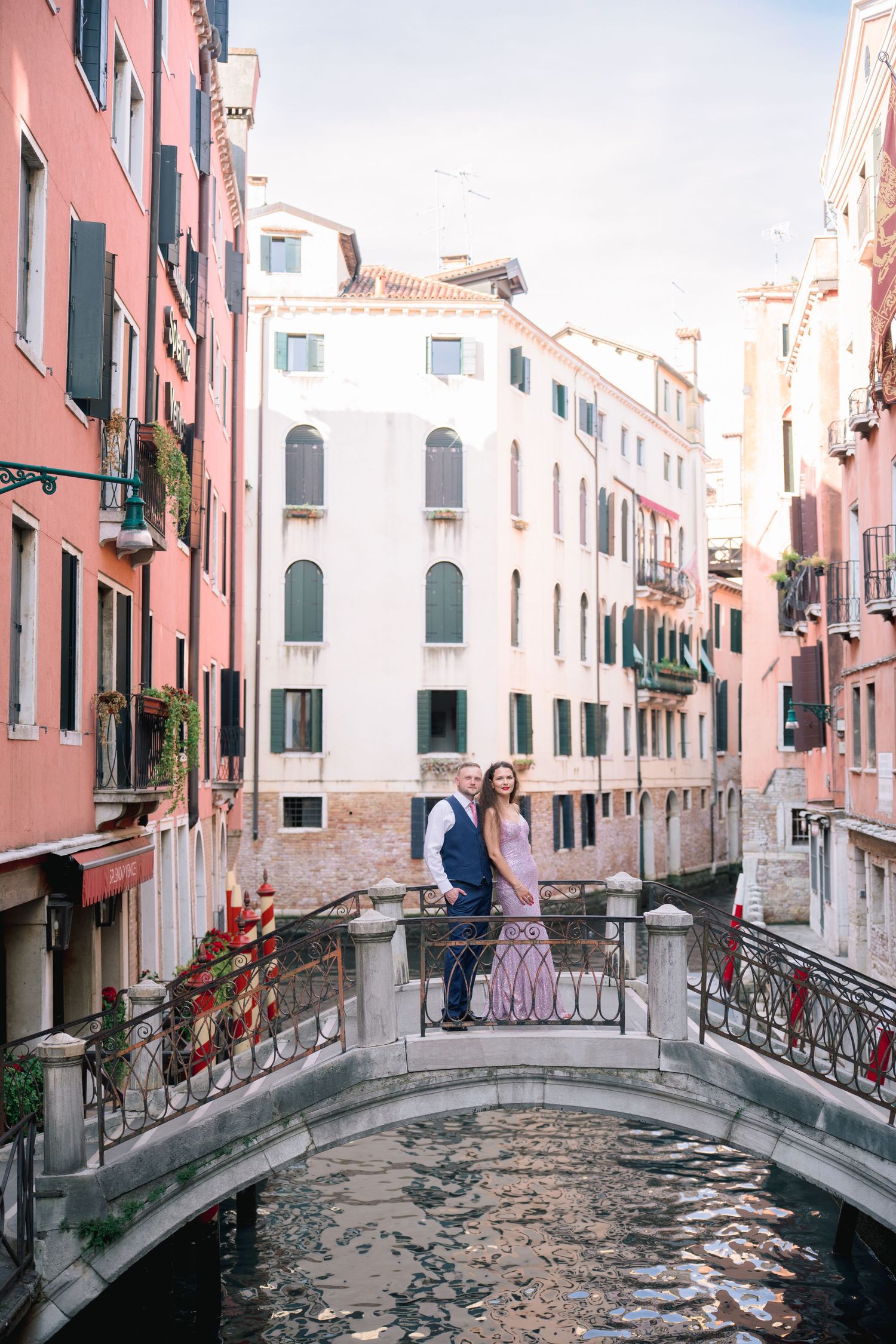 Couple embracing on a charming stone bridge over a Venetian canal, surrounded by colorful historic buildings in Venice, Italy.