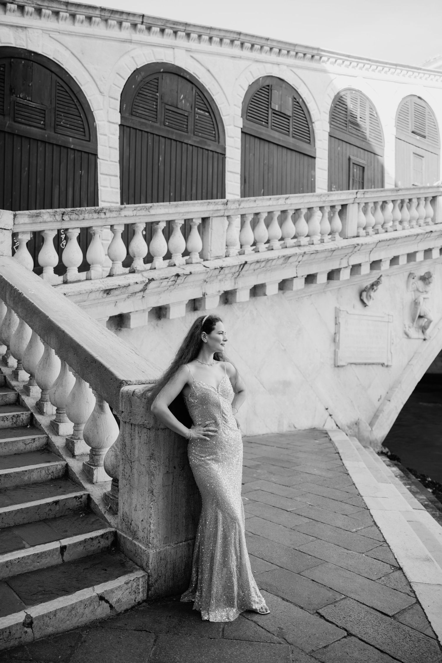 Elegant woman in a sequin gown posing by the Rialto Bridge in Venice, black and white photography.