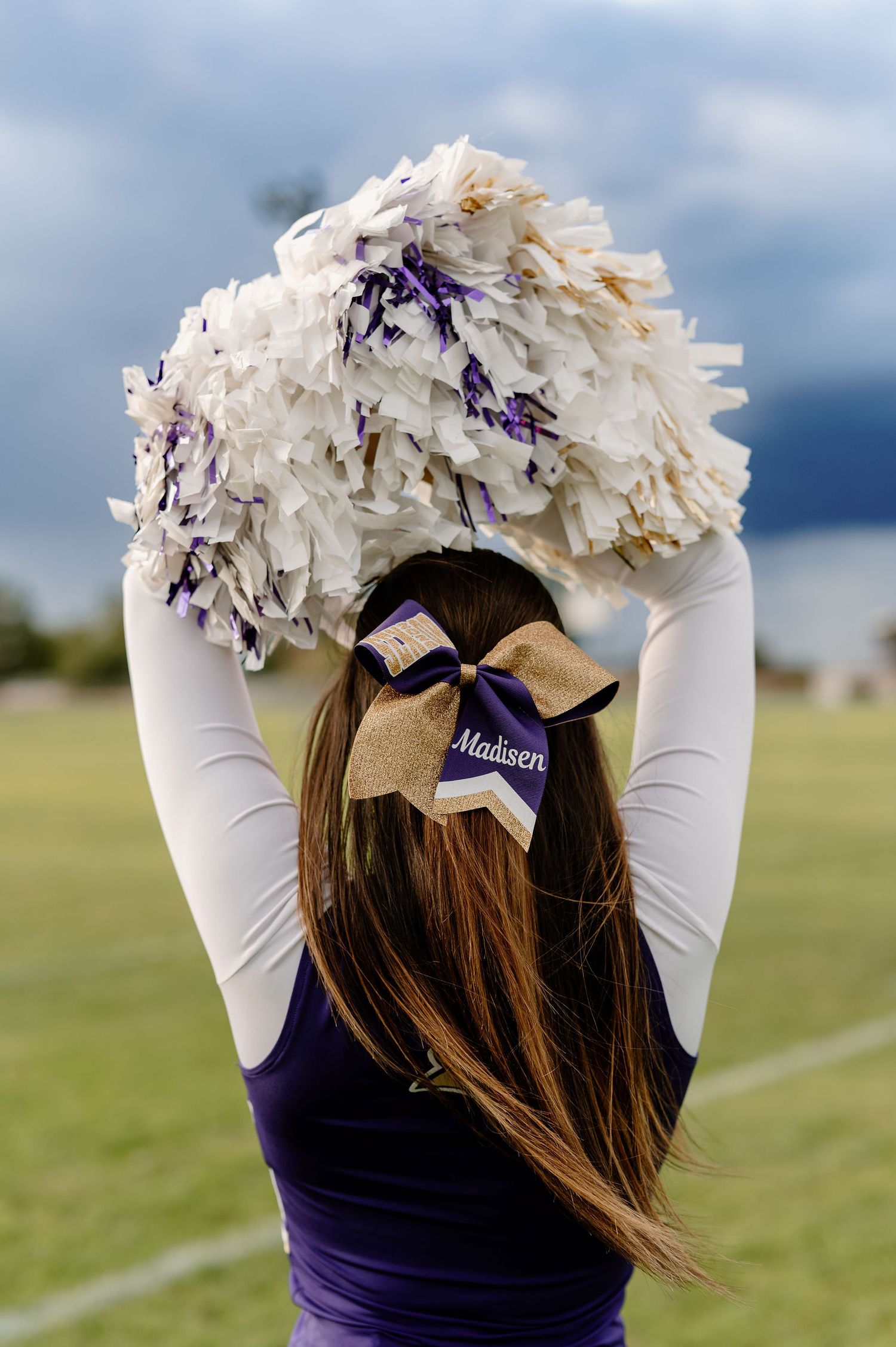 A 2026 senior on her high school football field in her cheer uniform with poms